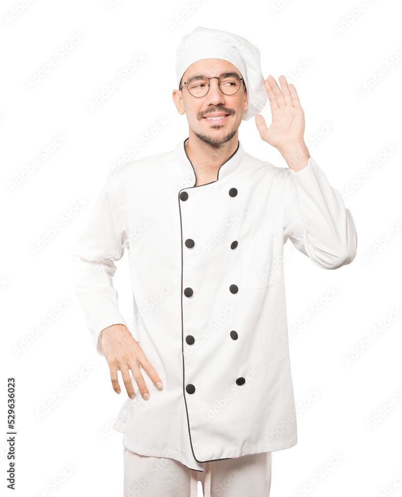 Happy young chef smiling and making a gesture of trying to hear something Happy young chef smiling and making a gesture of trying to hear something