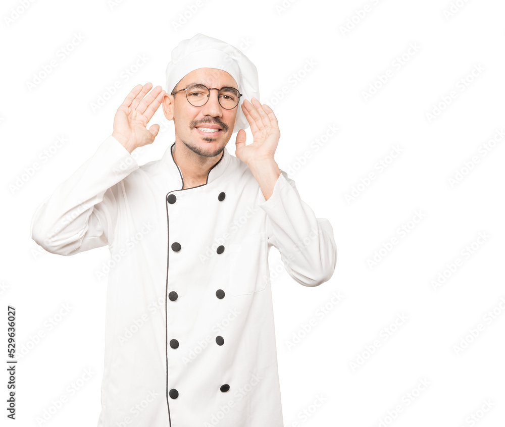 Happy young chef smiling and making a gesture of trying to hear something Happy young chef smiling and making a gesture of trying to hear something