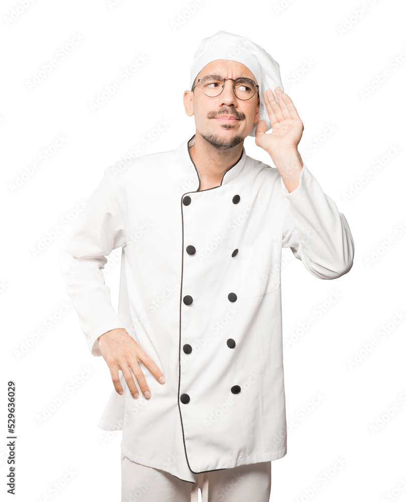 Concentrated young chef making a gesture of trying to hear something Concentrated young chef making a gesture of trying to hear something