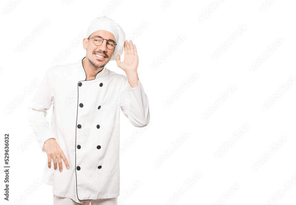 Happy young chef smiling and making a gesture of trying to hear something Happy young chef smiling and making a gesture of trying to hear something