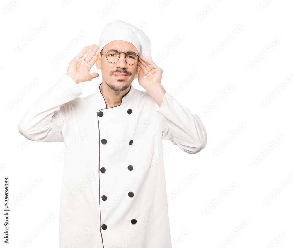 Concentrated young chef making a gesture of trying to hear something Concentrated young chef making a gesture of trying to hear something