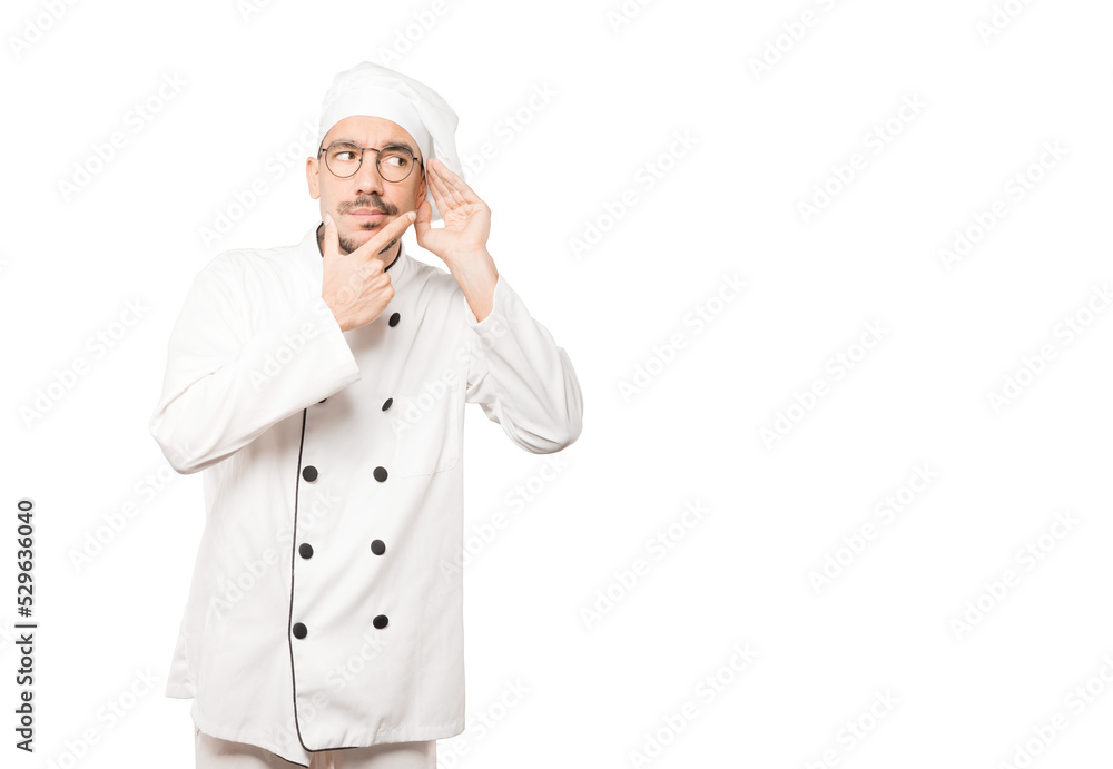 Concentrated young chef making a gesture of trying to hear something Concentrated young chef making a gesture of trying to hear something