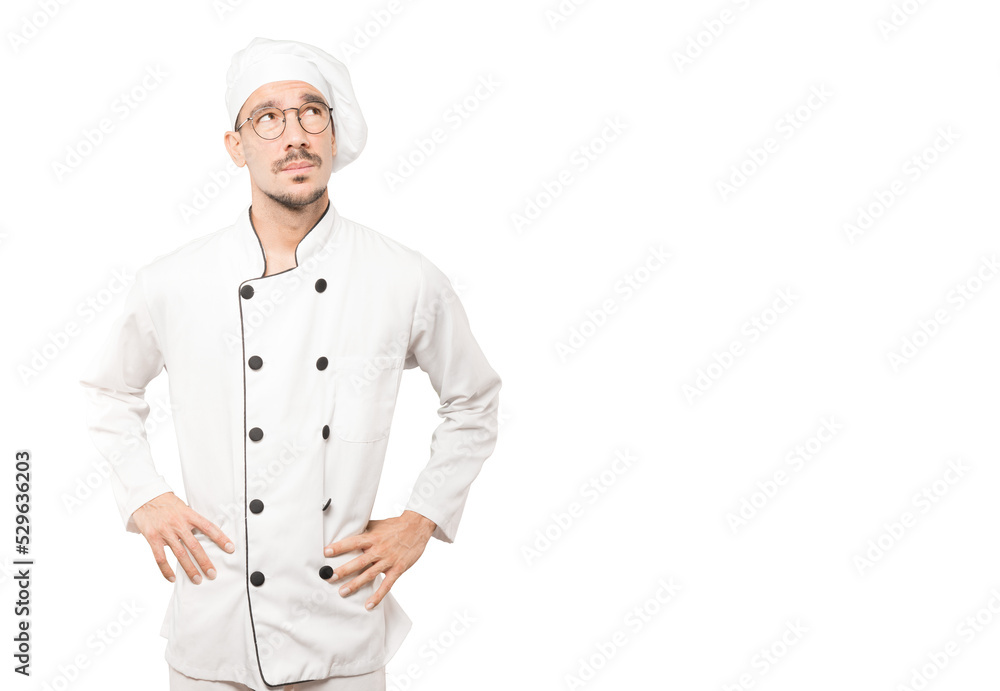 Serious young chef looking against background