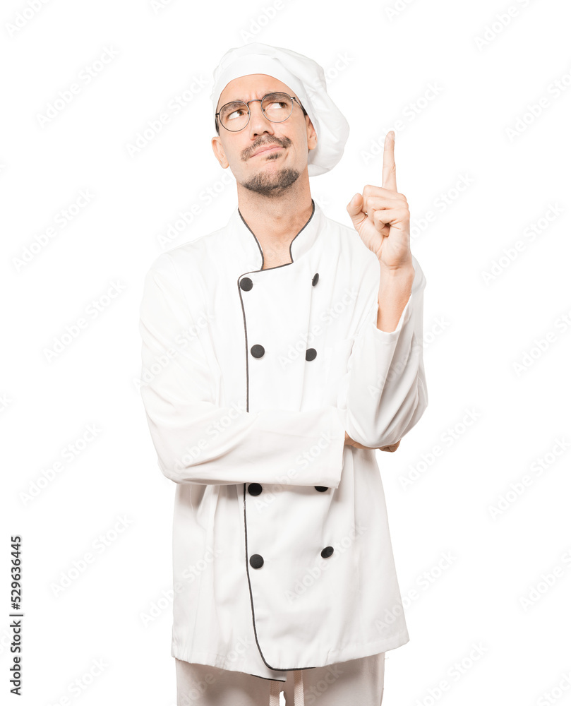Hesitant young chef pointing up with his finger Hesitant young chef pointing up with his finger