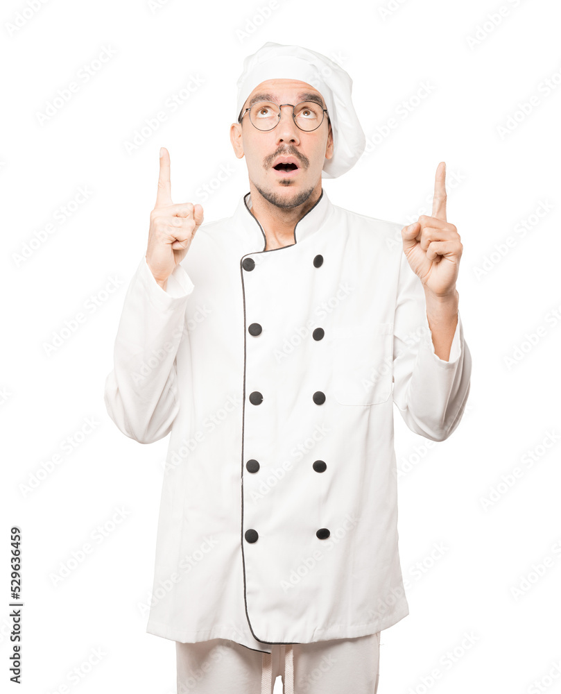 Amazed young chef pointing up with his finger Amazed young chef pointing up with his finger