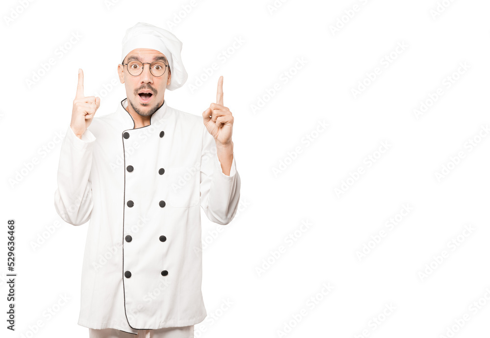 Amazed young chef pointing up with his finger Amazed young chef pointing up with his finger