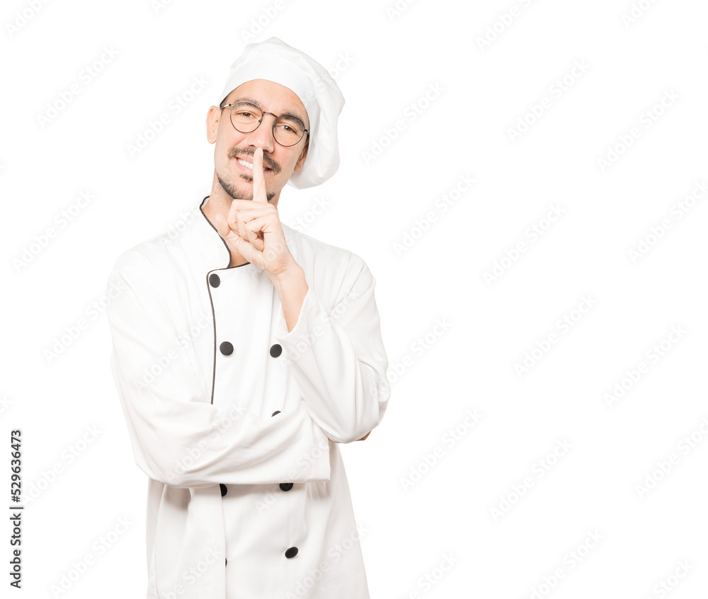 Happy young chef asking for silence gesturing with his finger Happy young chef asking for silence gesturing with his finger