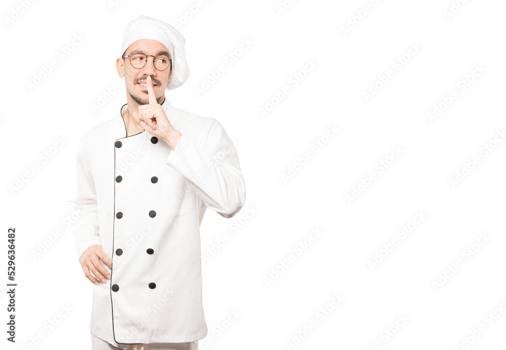 Happy young chef asking for silence gesturing with his finger