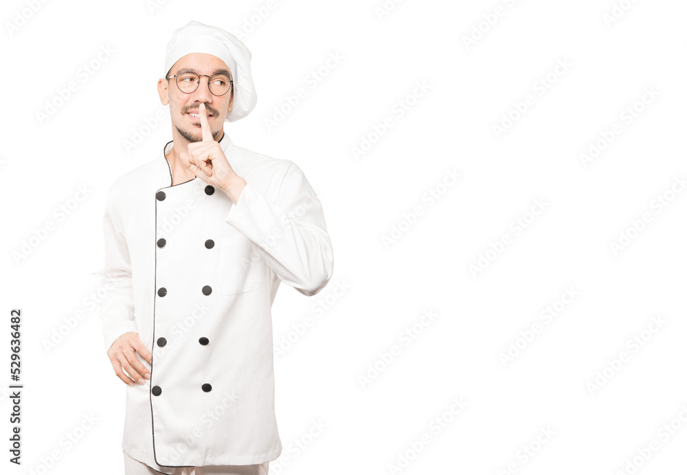 Happy young chef asking for silence gesturing with his finger Happy young chef asking for silence gesturing with his finger
