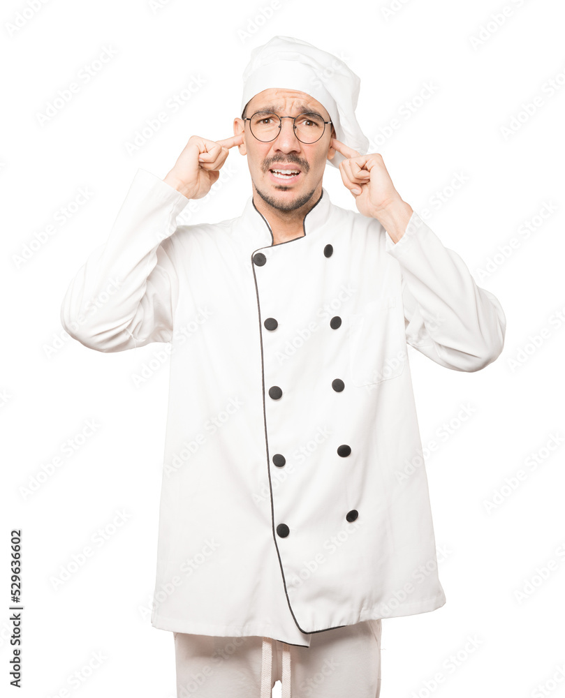 Concerned young chef worried about loud noises and covering his ears Concerned young chef worried about loud noises and covering his ears