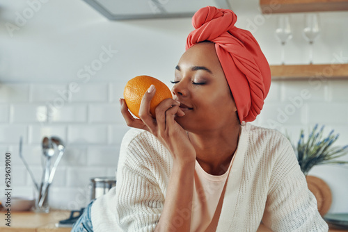 Canvas Print Attractive African woman in traditional headwear smelling oranges while standing