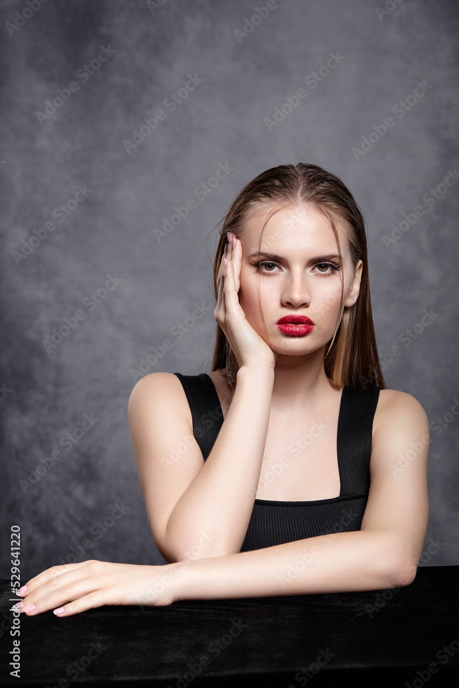 Beauty portrait of young woman sit at the black table on gray background. Beauty portrait of young woman sit at the black table on gray background.