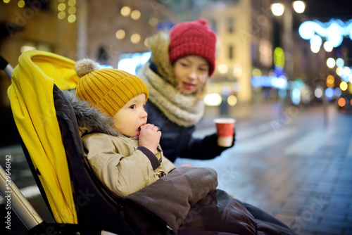Cute toddler boy and his sister having fun on Christmas time in Vilnius, Lithuania. Small child in a stroller on Christmas market.