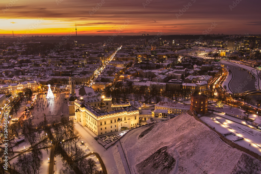 Fototapeta premium Beautiful Vilnius city panorama in winter with snow covered houses, churches and streets. Aerial evening view. Winter city scenery in Lithuania.