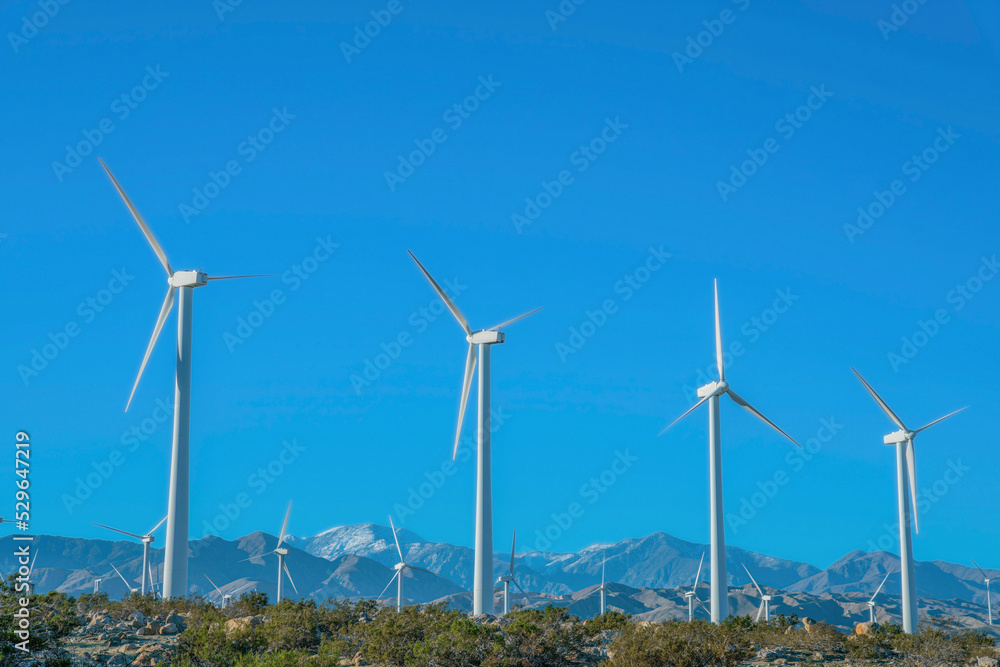 Fototapeta premium Windmills with three sharp blades against mountains and blue sky background