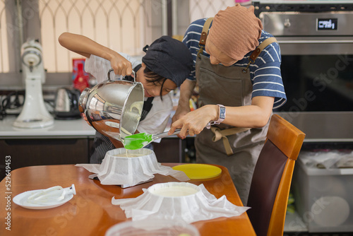 Mother with young son wearing apron pouring cream from mixing bowl into baking mold.