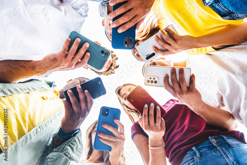 Teens in circle holding smart mobile phones - Multicultural young people using cellphones outside - Teenagers addicted to new technology concept photo