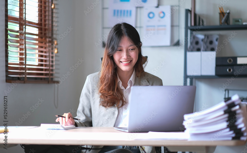 Beautiful Asian businesswoman analyzes charts using laptop calculator at the office. Beautiful Asian businesswoman analyzes charts using laptop calculator at the office.