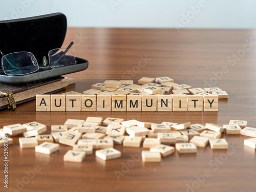 autoimmunity word or concept represented by wooden letter tiles on a wooden table with glasses and a book photo