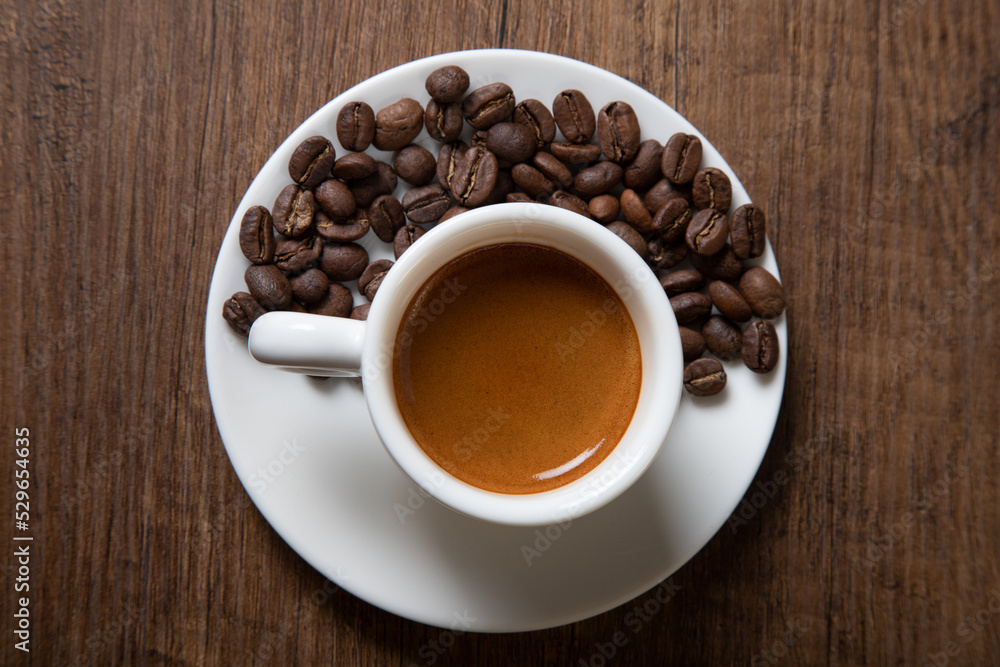 White cup of espresso with coffee beans on wooden background White cup of espresso with coffee beans on wooden background