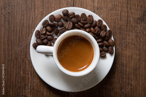 White cup of espresso with coffee beans on wooden background