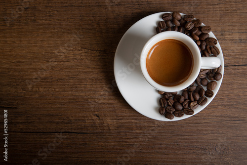 White cup of espresso with coffee beans on wooden background