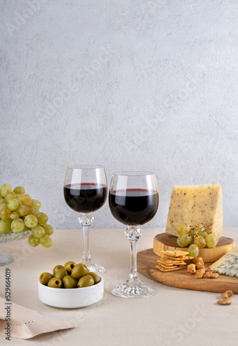 Glasses of red wine with grapes and cheese on light table background. Red wine with cheese and fruits. Space for text