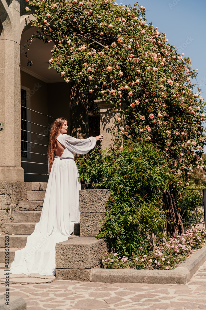 Obraz premium a beautiful woman in a white flowing long dress stay near a beautiful field with pink flowers rear view