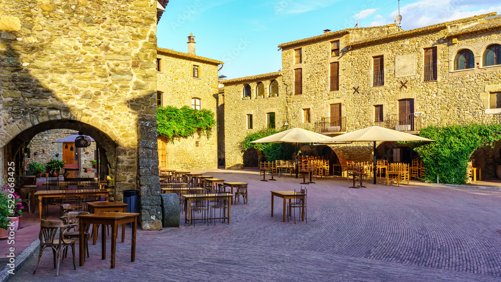 Central Square of the medieval village of Monells with its stone houses and arches in the buildings, Girona, Spain.