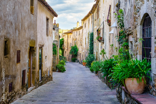 Beautiful alley with old stone houses and pots on the street with plants and flowers, Monells, Girona, Catalonia. photo