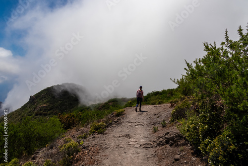 Woman with backpack descending Pico Verde with view on the Teno mountain massif, Tenerife, Canary Islands, Spain, Europe. Hiking trail between village Masca and Santiago. Entering the fog