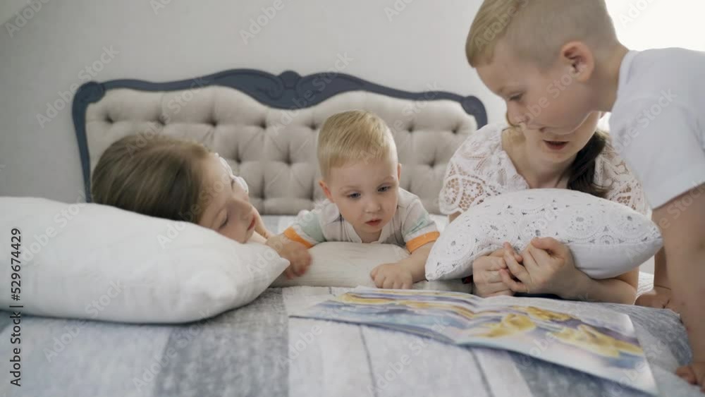 Children lie on the bed in the bedroom, mother reads a book to them. They lie on pillows. Education concept. Children lie on the bed in the bedroom, mother reads a book to them. They lie on pillows. Education concept.