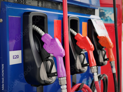 man hand holding a green gas nozzle. A man's hand is pulling the fuel dispenser out of the red meter cabinet. E20 uses a green fuel nozzle. Woman is holding a gasoline fuel pistol at gas station.
