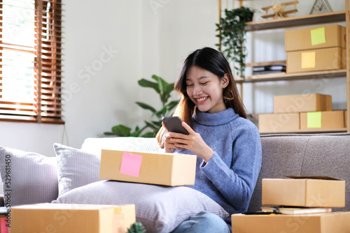 Happy young Asian woman entrepreneur, Smile for sales success after checking order from online shopping store in a smartphone at home office, Concept of merchant business online and eCommerce © wichayada