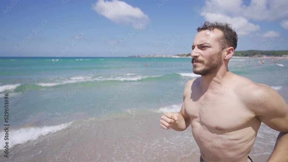 Stable sportsman running in the sea in slow motion.
Muscular athletic man running on beach on summer day.
