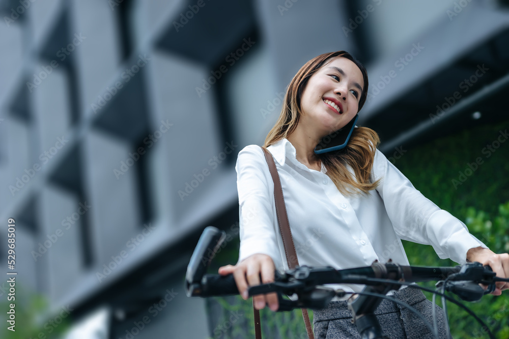 Young Asian businesswoman wearing helmet and standing on a city street with bicycle looking at phone.