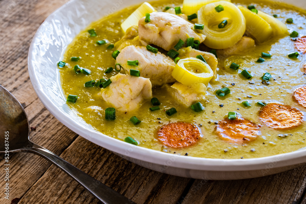 Bowl of hot leek soup with chicken meat on wooden table
Bowl of hot leek soup with chicken meat on wooden table