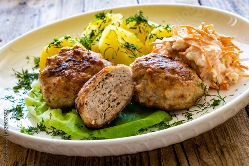 Fried meatballs with boiled potatoes and carrot salad on wooden table 