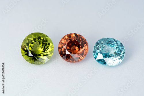 Green peridot, aka chrysolite or olivine. Dark orange and electric turquoise blue color natural zircon gemstones settings in one photo on white paper background. front view. Facets details. Gemology.