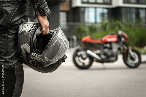 Fototapeta Biker walks to motorcycle holding helmet in hand