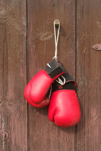 Old worn leather red boxing gloves hang against the background of the wooden in brown