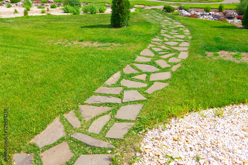 Garden path made of flat stone among green grass.