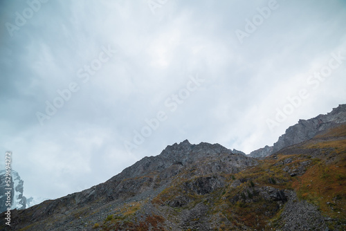 Gloomy autumn landscape with large mountain with sharp rocks on top under gray cloudy sky. Dark atmospheric scenery with high rocky mountain in fading autumn colors and pointy peak in overcast weather