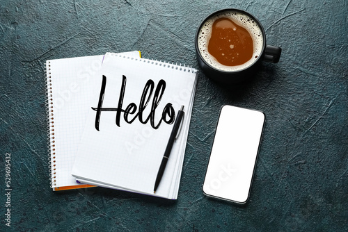 Notebook with word HELLO, cup of coffee, phone and pen on dark background photo