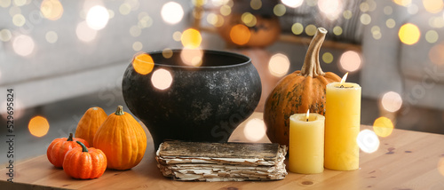 Witch's cauldron with old book, candles and pumpkins on table in room
