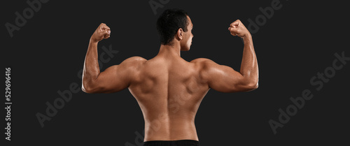 Sporty muscled man on dark background, back view