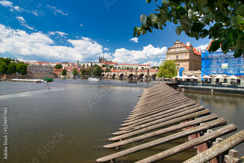 Photography Look over Vltava river to Charles bridge, Prague Castle in background under blus sky with white clouds