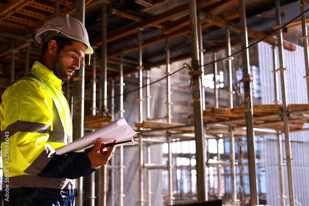 Handsome engineer with green safety jacket working at construction site line, chief engineer check the job progress with the drawing