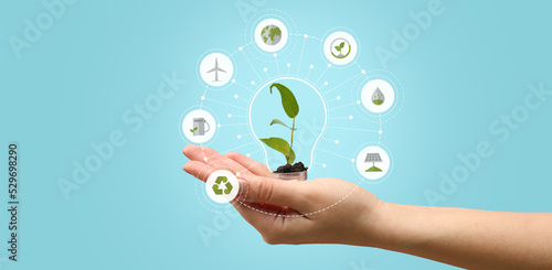 Female hand holding light bulb with plant inside and different digital icons on light blue background. Ecology concept © Pixel-Shot