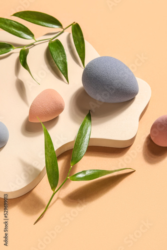 Stand with makeup sponges and plant leaves on beige background